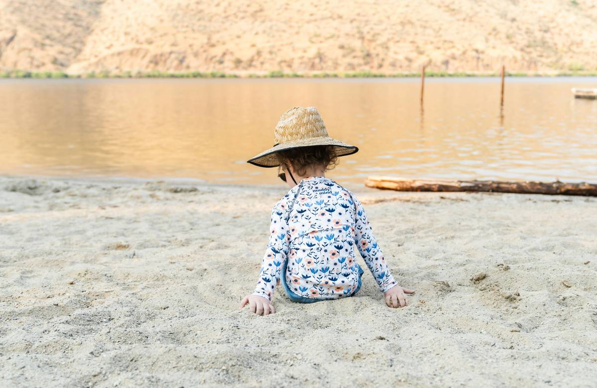mother applying baby skin care sunscreen on toddler at beach